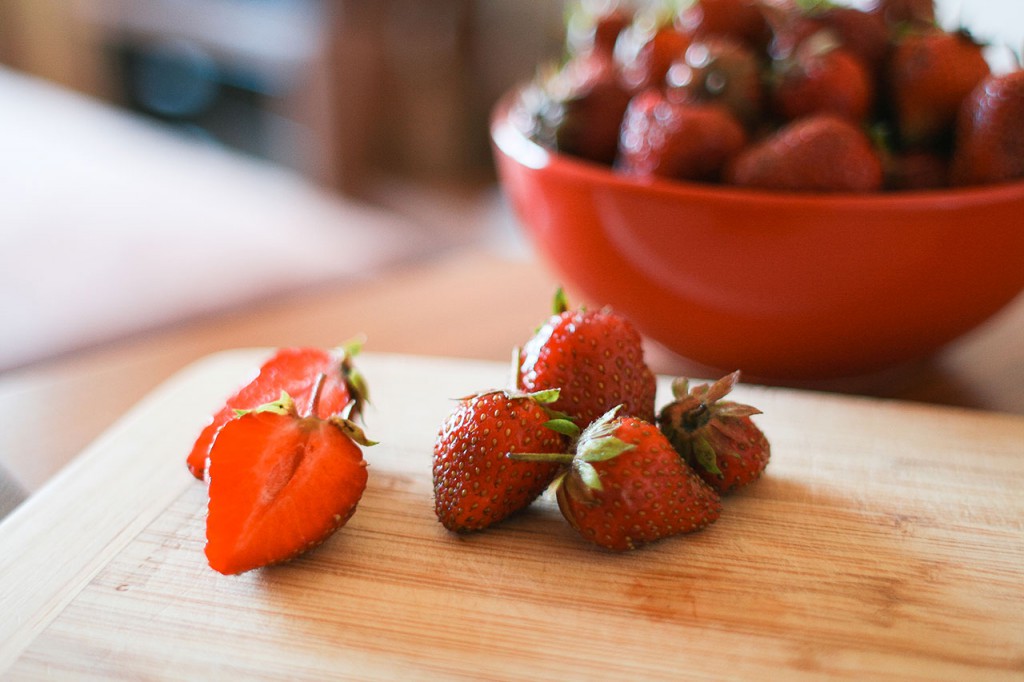 A bowl of strawberries and some cut up strawberries