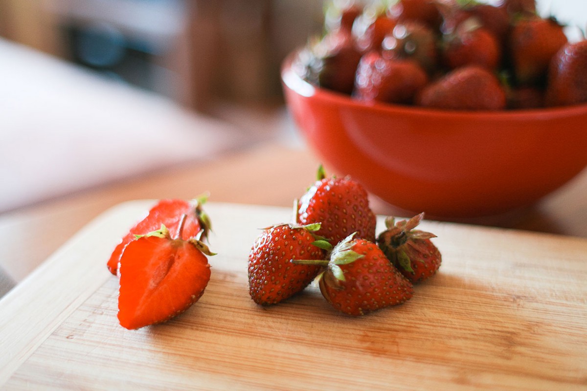 A bowl of strawberries and some cut up strawberries