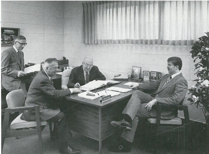 Three men sitting at a table in front of papers.