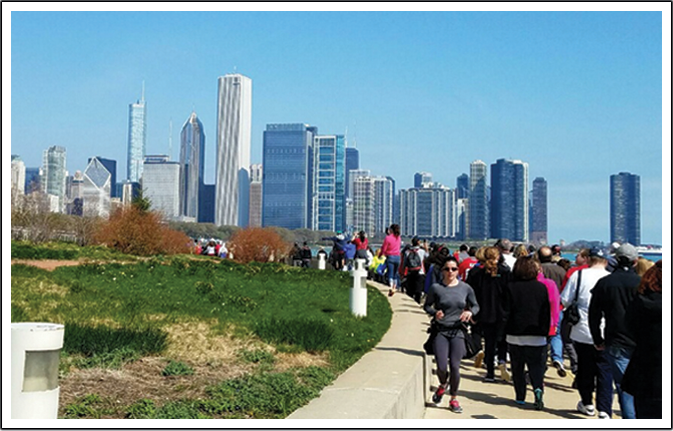 A group of people walking on the sidewalk near a park.